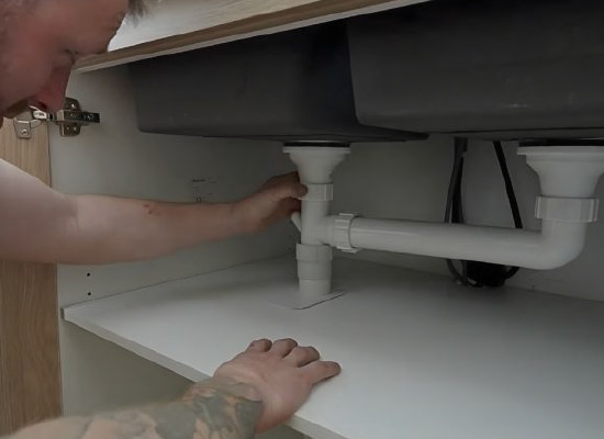 Plumber inspecting pipework under a sink for hidden leaks